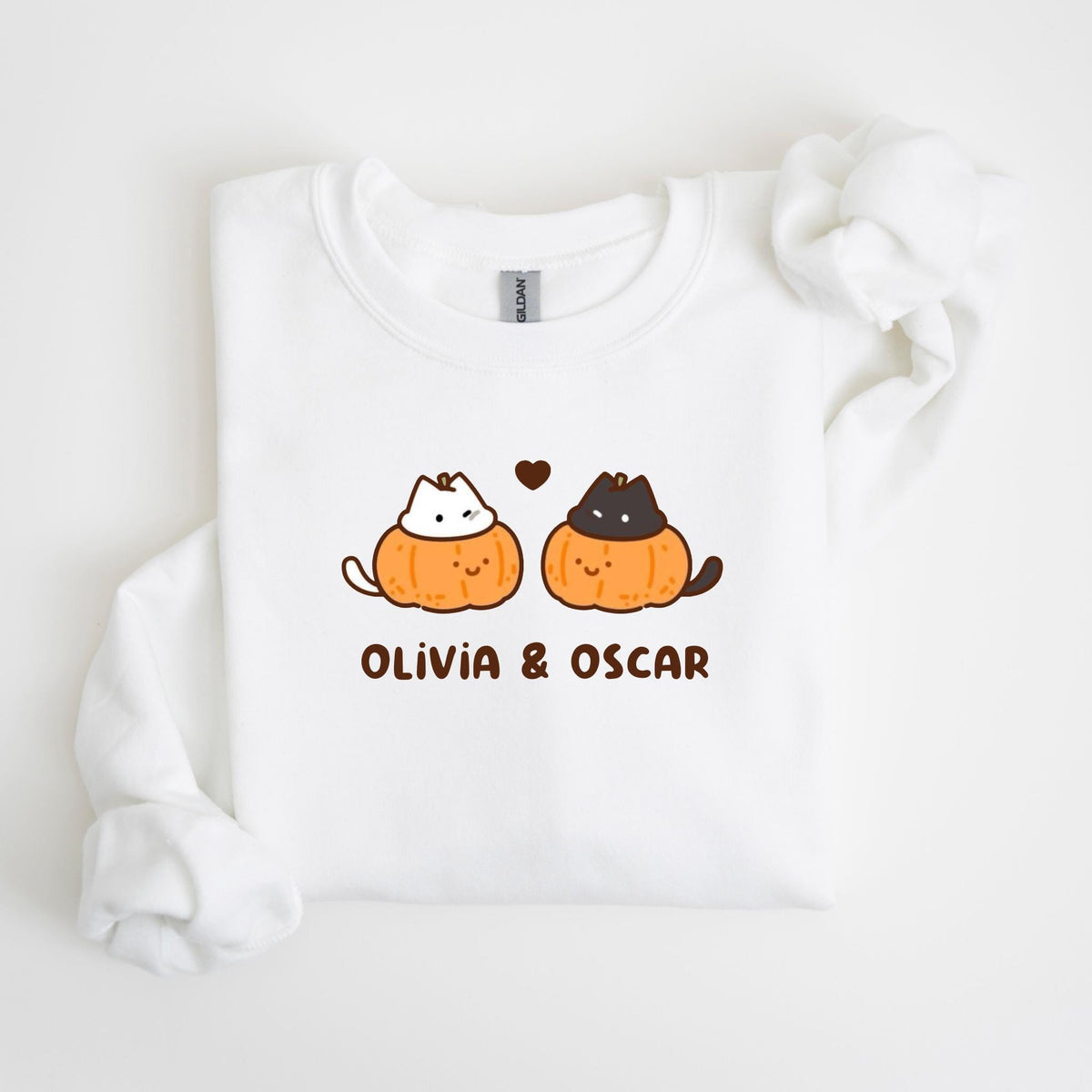 May include: White sweatshirt featuring a graphic of two cartoon cats in pumpkin costumes, with the text "OLIVIA & OSCAR" in brown. The cats have white and black fur, and a brown heart is above them.