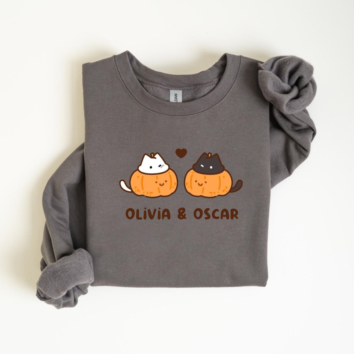 May include: Dark gray sweatshirt featuring a graphic of two cats inside orange pumpkins, with a small brown heart above them. The text "OLIVIA & OSCAR" is printed below the pumpkins. The sweatshirt has long sleeves.