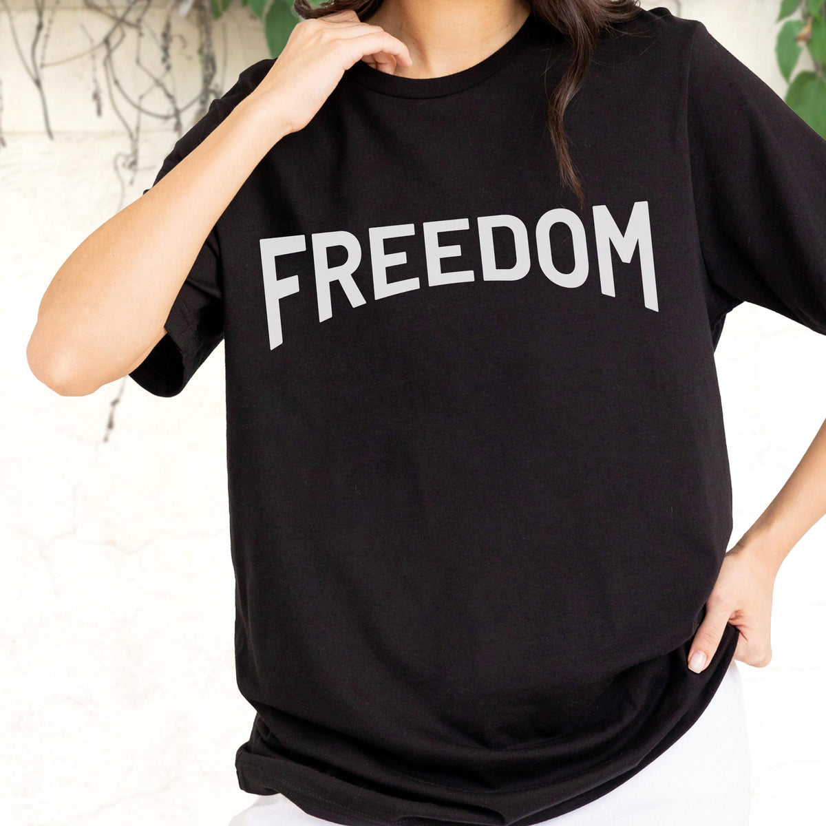 May include: Black t-shirt with the word "FREEDOM" printed in large, white, capital letters across the chest. The shirt has short sleeves and a crew neck. The person is wearing white pants.