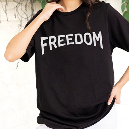 May include: Black t-shirt with the word "FREEDOM" printed in large, white, capital letters across the chest. The shirt has short sleeves and a crew neck. The person is wearing white pants.