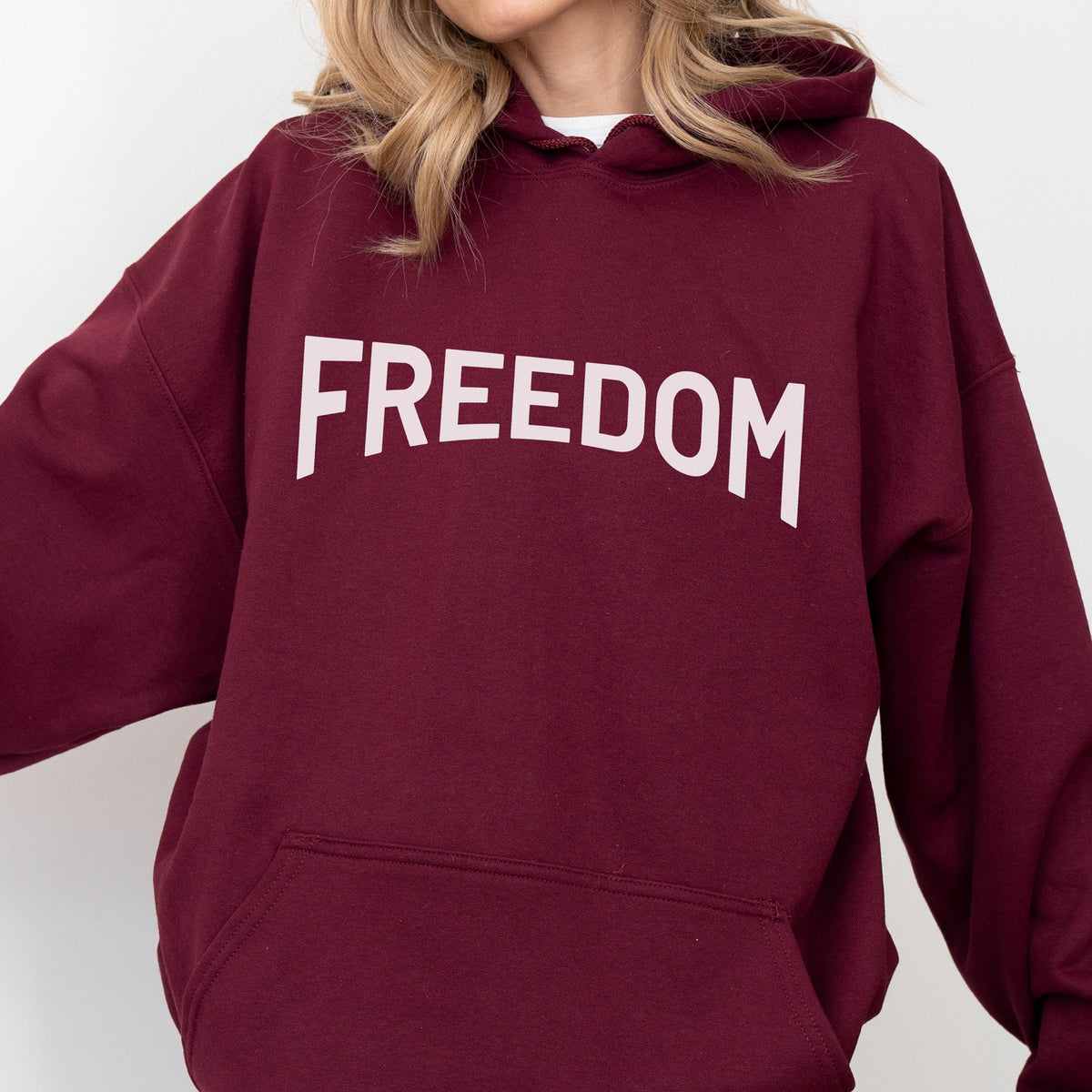 May include: A maroon hoodie with the word "FREEDOM" printed in large, white capital letters across the chest. The hoodie has a drawstring hood and a front pocket. The sleeves are long and the material appears to be a soft fabric.