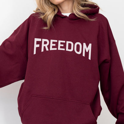 May include: A maroon hoodie with the word "FREEDOM" printed in large, white capital letters across the chest. The hoodie has a drawstring hood and a front pocket. The sleeves are long and the material appears to be a soft fabric.