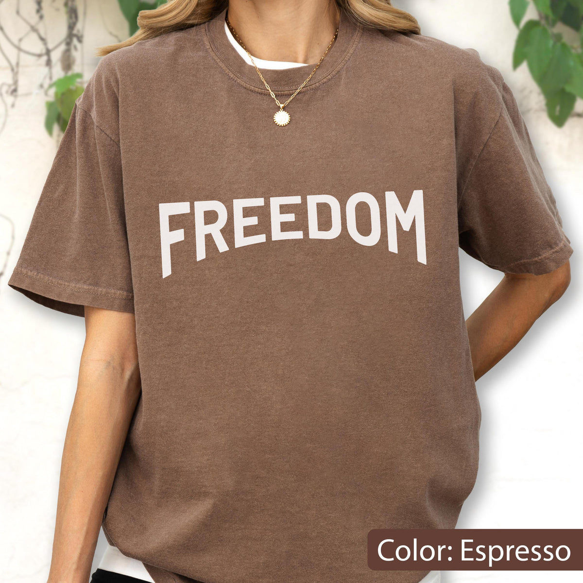 May include: Espresso-colored t-shirt with the word "FREEDOM" in large white letters across the chest. The shirt has short sleeves and a relaxed fit. The color is described as Espresso.