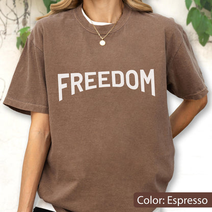May include: Espresso-colored t-shirt with the word "FREEDOM" in large white letters across the chest. The shirt has short sleeves and a relaxed fit. The color is described as Espresso.