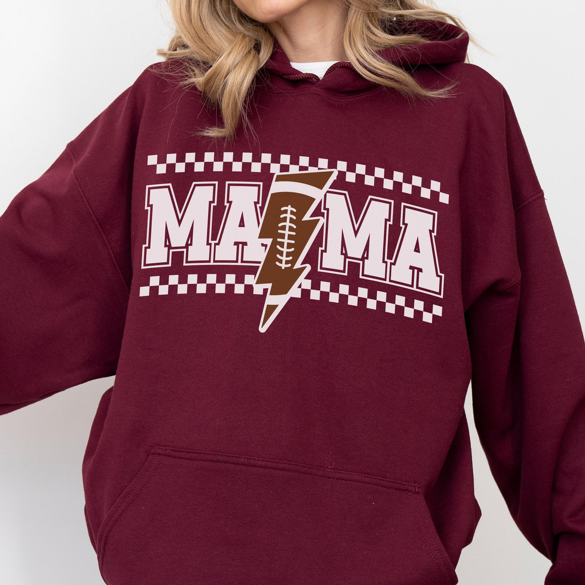 May include: A maroon hoodie with the word "MAMA" in white block letters, with a brown football-shaped lightning bolt in the center. The design is framed by a white and black checkered pattern. The hoodie has a hood and a front pocket.