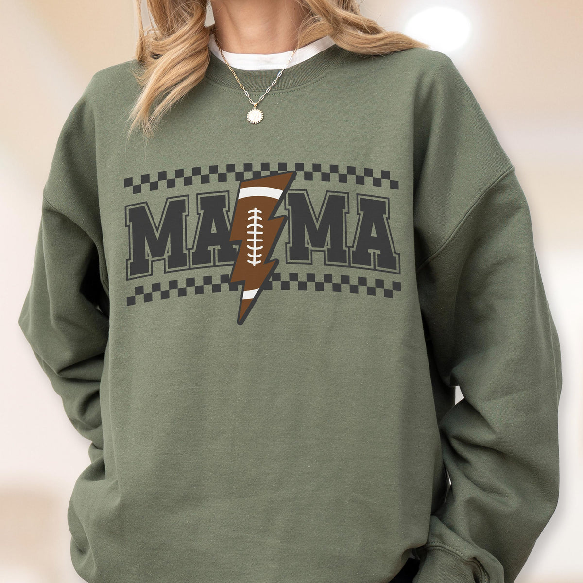 May include: Olive green sweatshirt with the word "MAMA" in a block letter design. The letters are outlined in black and have a checkered pattern above and below. A brown football-shaped lightning bolt is in the center.