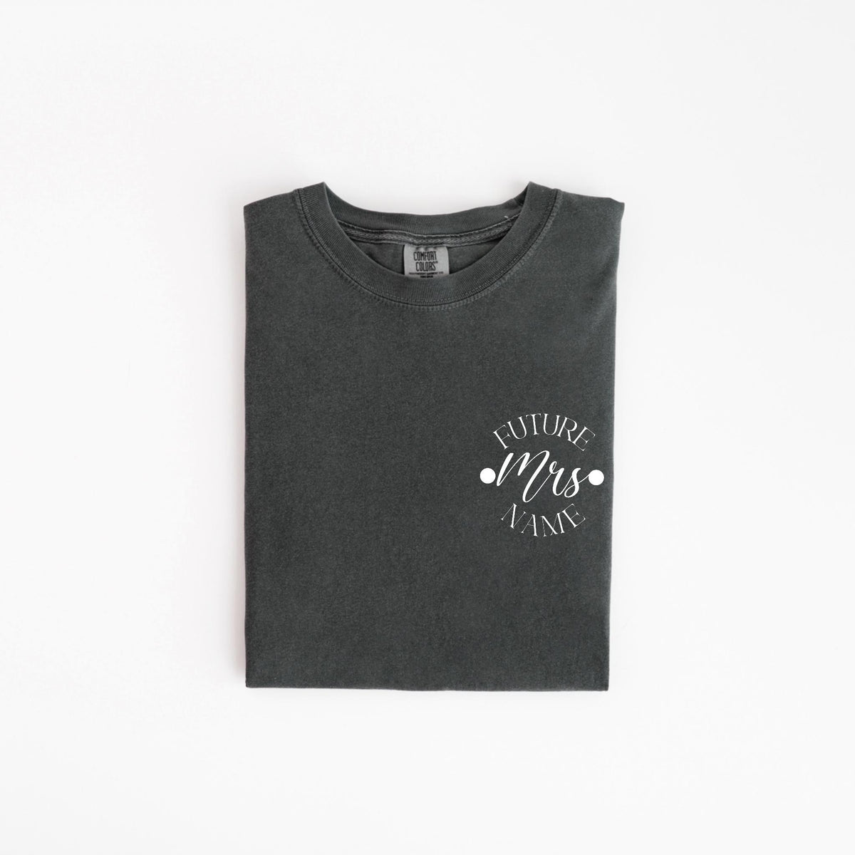 May include: A dark gray t-shirt with the words "FUTURE Mrs. NAME" printed in white script. The text is centered on the left chest area. The shirt is folded neatly on a white background.