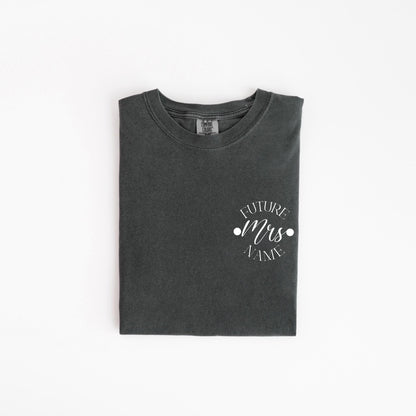 May include: A dark gray t-shirt with the words "FUTURE Mrs. NAME" printed in white script. The text is centered on the left chest area. The shirt is folded neatly on a white background.