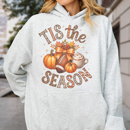 May include: Light gray hoodie with a fall-themed graphic. The design includes pumpkins, a football, a bow, and a coffee cup. The text reads "Tis the Season" in a mix of plaid and leopard print.