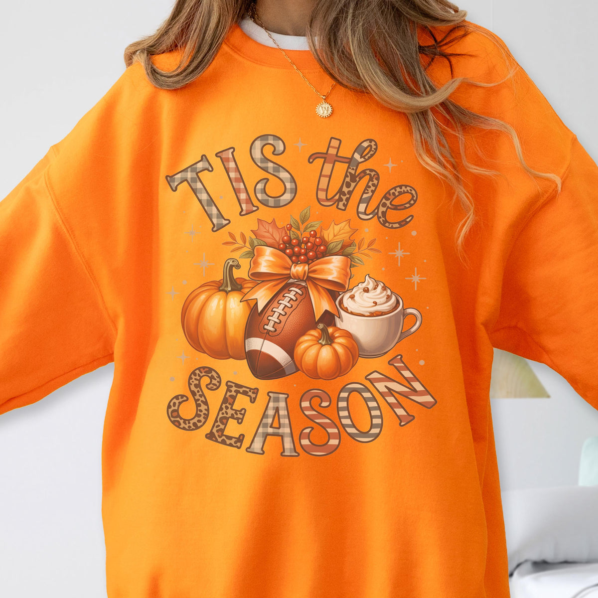 May include: Orange sweatshirt with a fall-themed graphic. The design includes pumpkins, a football, a cup of whipped cream, and the text "TIS the SEASON" in a decorative font.