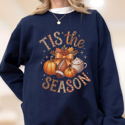 May include: Navy blue sweatshirt with a fall-themed graphic. The design includes pumpkins, a football, a bow, and a cup of whipped cream. The text "Tis the Season" is incorporated into the design.