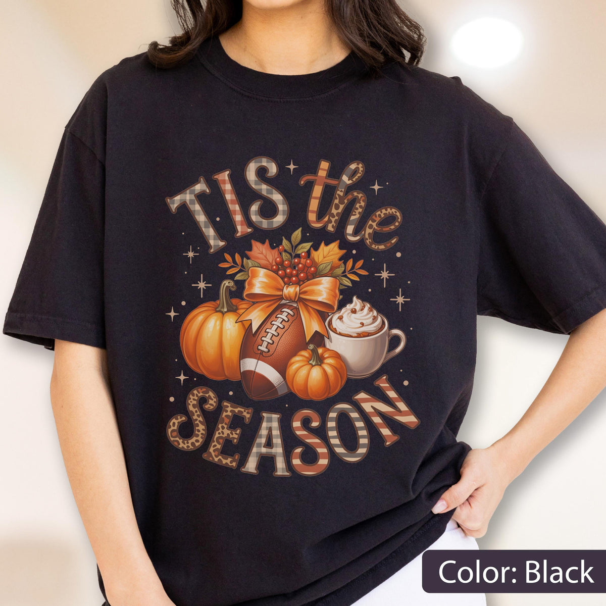 May include: Black t-shirt with a fall-themed graphic. The design includes pumpkins, a football, a coffee cup, and the text "Tis the Season." The text and images have a mix of patterns and colors, including orange, brown, and tan.
