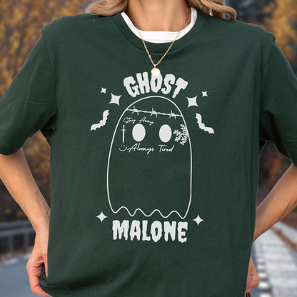 May include: A dark green t-shirt featuring a white graphic of a ghost with barbed wire across the top, a small cross, a snowflake, and the text "GHOST MALONE" along with the phrases "Stay Away" and "Always Tired" printed in a white font.
