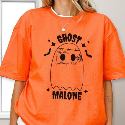 May include: An orange t-shirt featuring a black graphic of a ghost with barbed wire across its head, a sword, a snowflake, and the text "GHOST MALONE", "Stay Away", and "Always Tired" printed in black ink on the front of the garment.