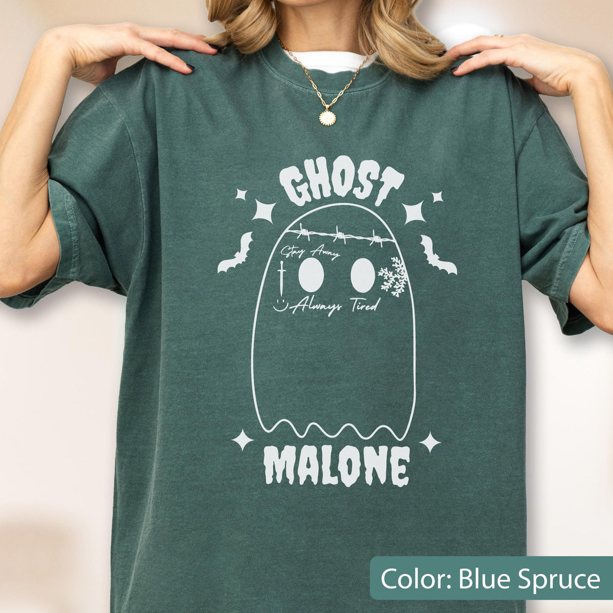 May include: Blue spruce-colored t-shirt with a white ghost graphic. The ghost design includes the word "GHOST" above the ghost, and the word "MALONE" below. The ghost has the words "Stay Away" and "Always Tired" on it.
