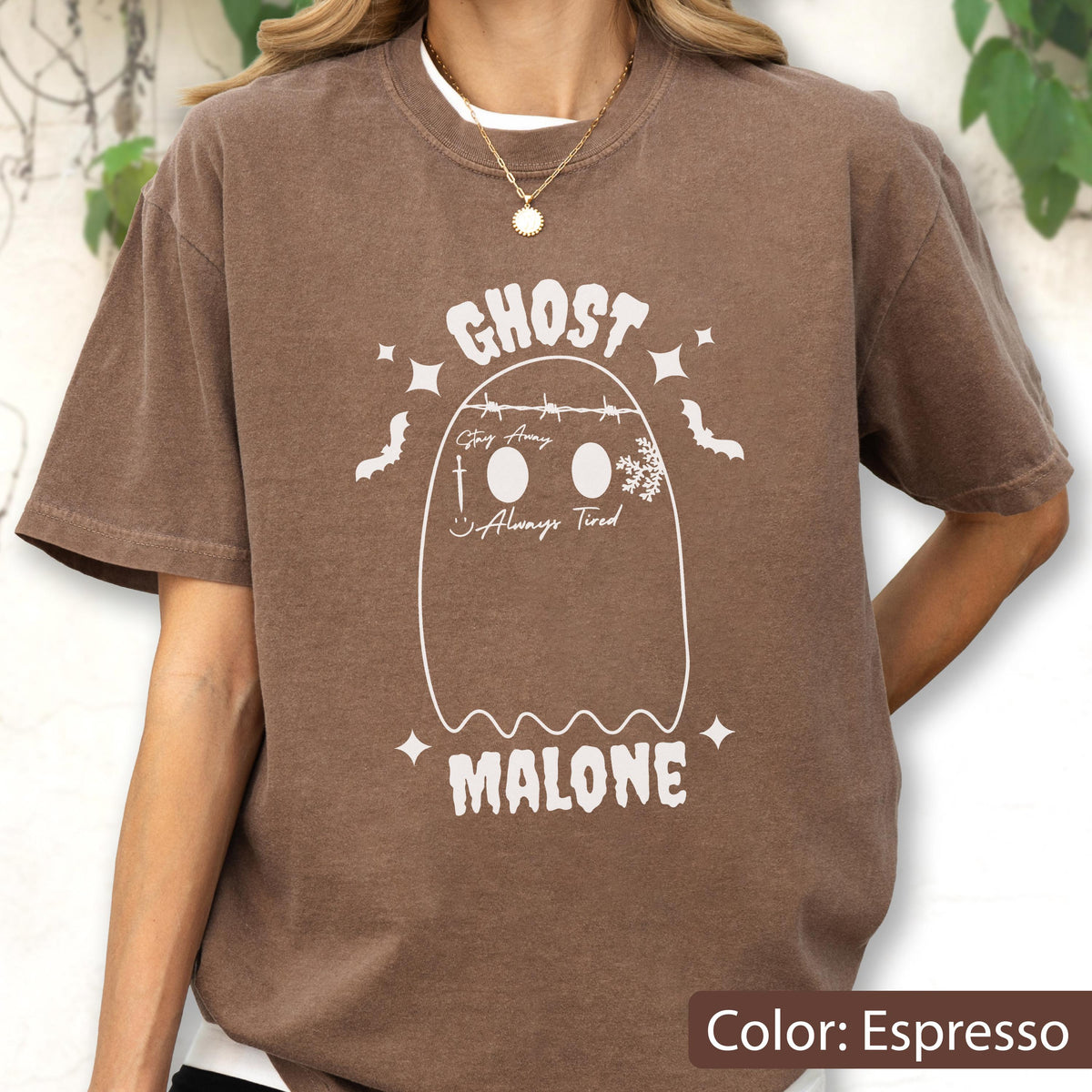 May include: Espresso-colored t-shirt featuring a white ghost design with the text "GHOST MALONE". The design includes bats, stars, and the phrases "Stay Away" and "Always Tired". The shirt has a crew neck and short sleeves.