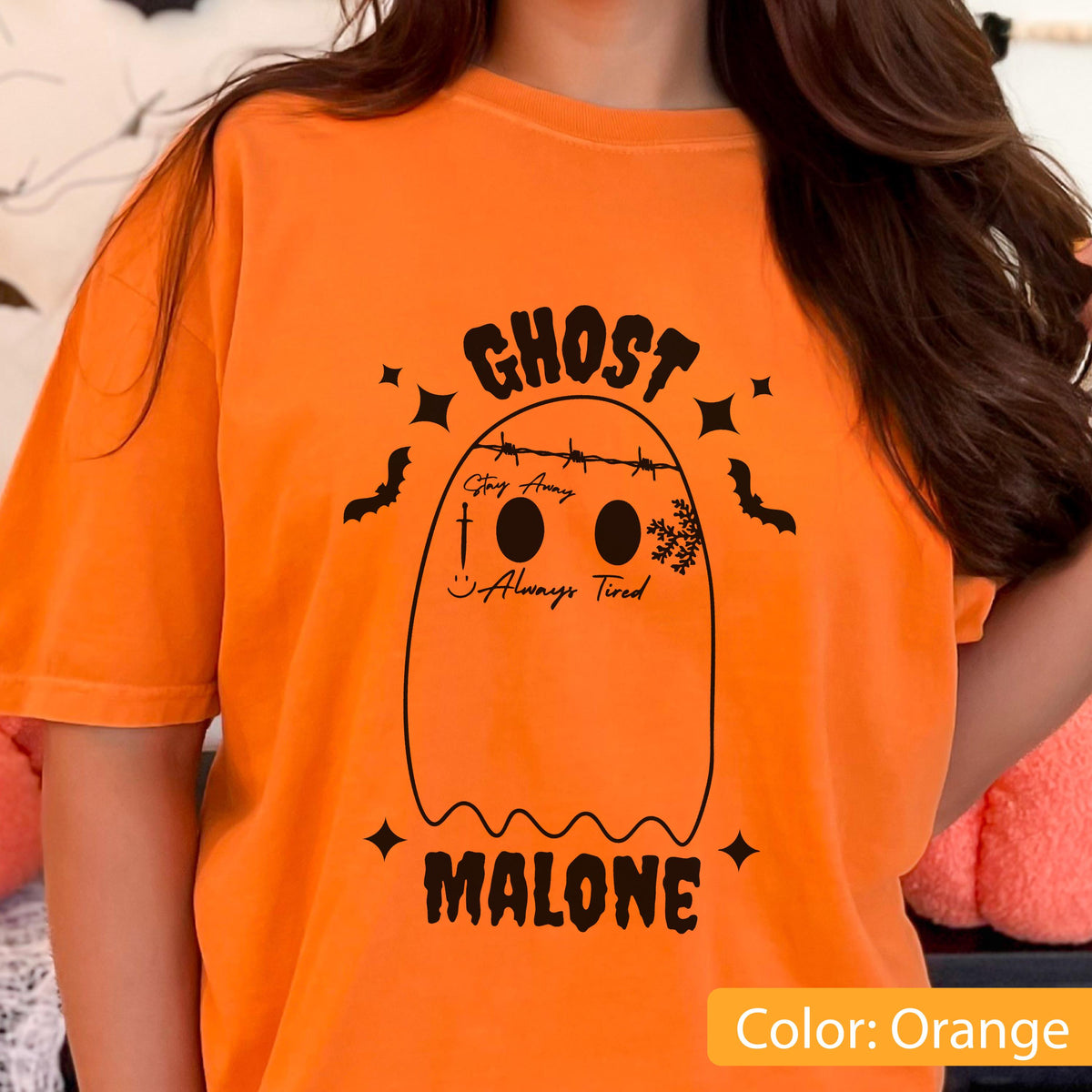 May include: Orange t-shirt with a black ghost graphic. The ghost design includes the words "Ghost Malone", "Stay Away", and "Always Tired". The shirt also features bats and stars.