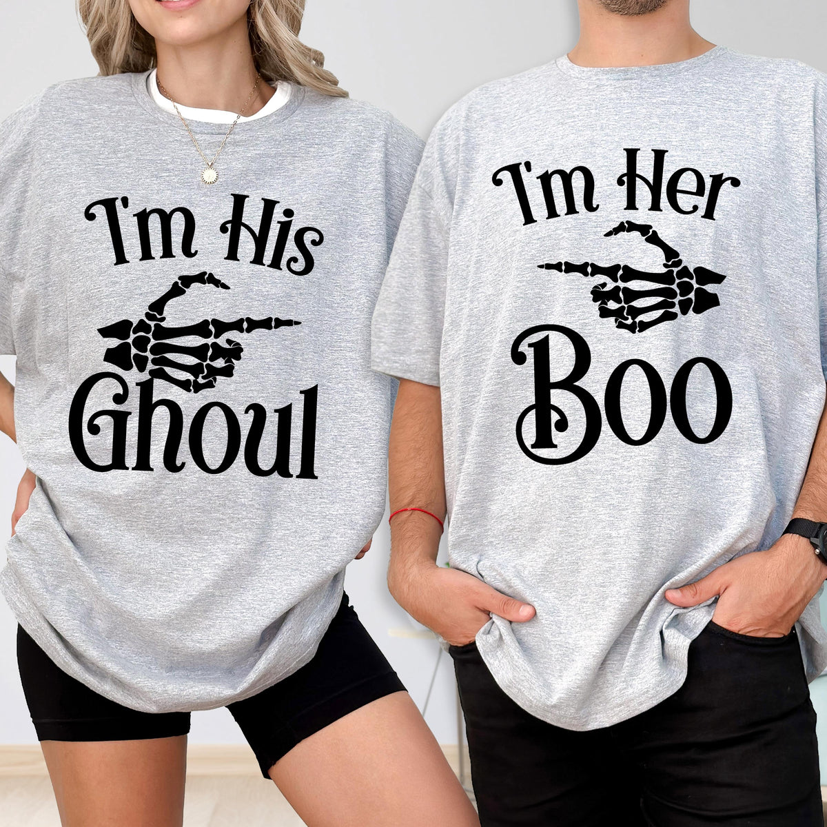 May include: Two light gray t-shirts featuring black text and skeleton hand graphics. The left shirt reads "I'm His Ghoul" with a skeleton hand pointing right. The right shirt reads "I'm Her Boo" with a skeleton hand pointing left.