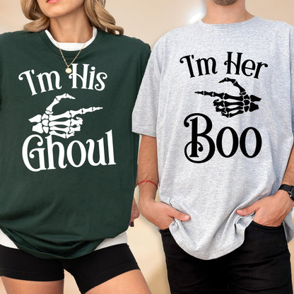 May include: A dark green t-shirt with white text reading I'm His Ghoul and a white skeleton hand graphic, paired with a light gray t-shirt with black text reading I'm Her Boo and a black skeleton hand graphic pointing to the side.