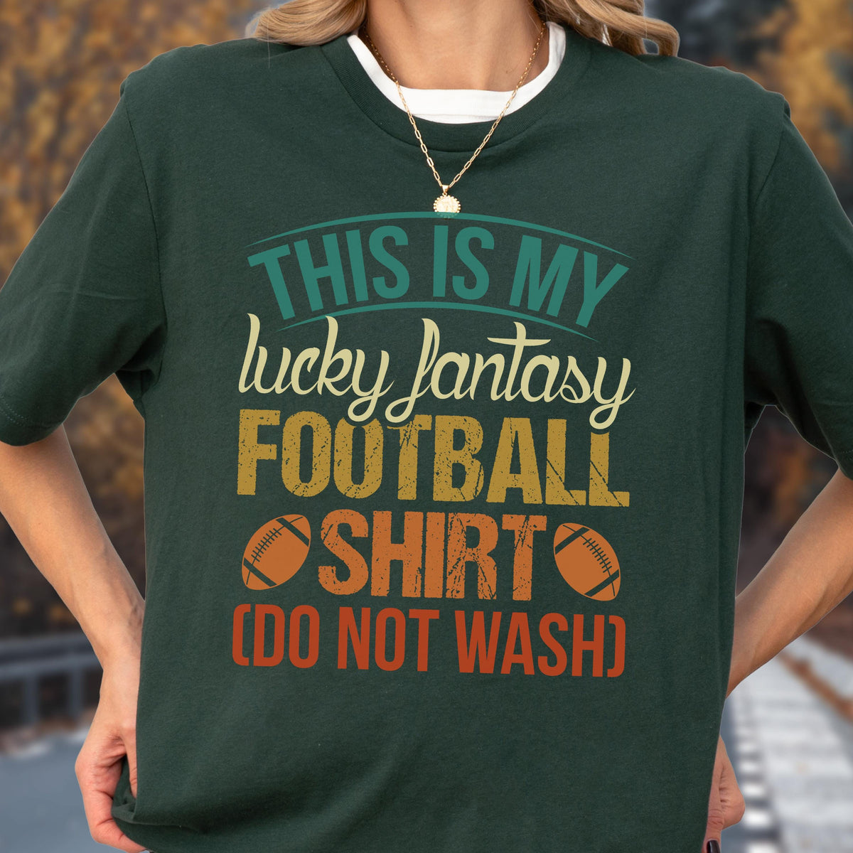 May include: A dark green short-sleeve t-shirt featuring a multi-colored graphic print that reads: THIS IS MY lucky fantasy FOOTBALL SHIRT (DO NOT WASH). The design includes two brown football illustrations and uses a distressed, vintage-style font.