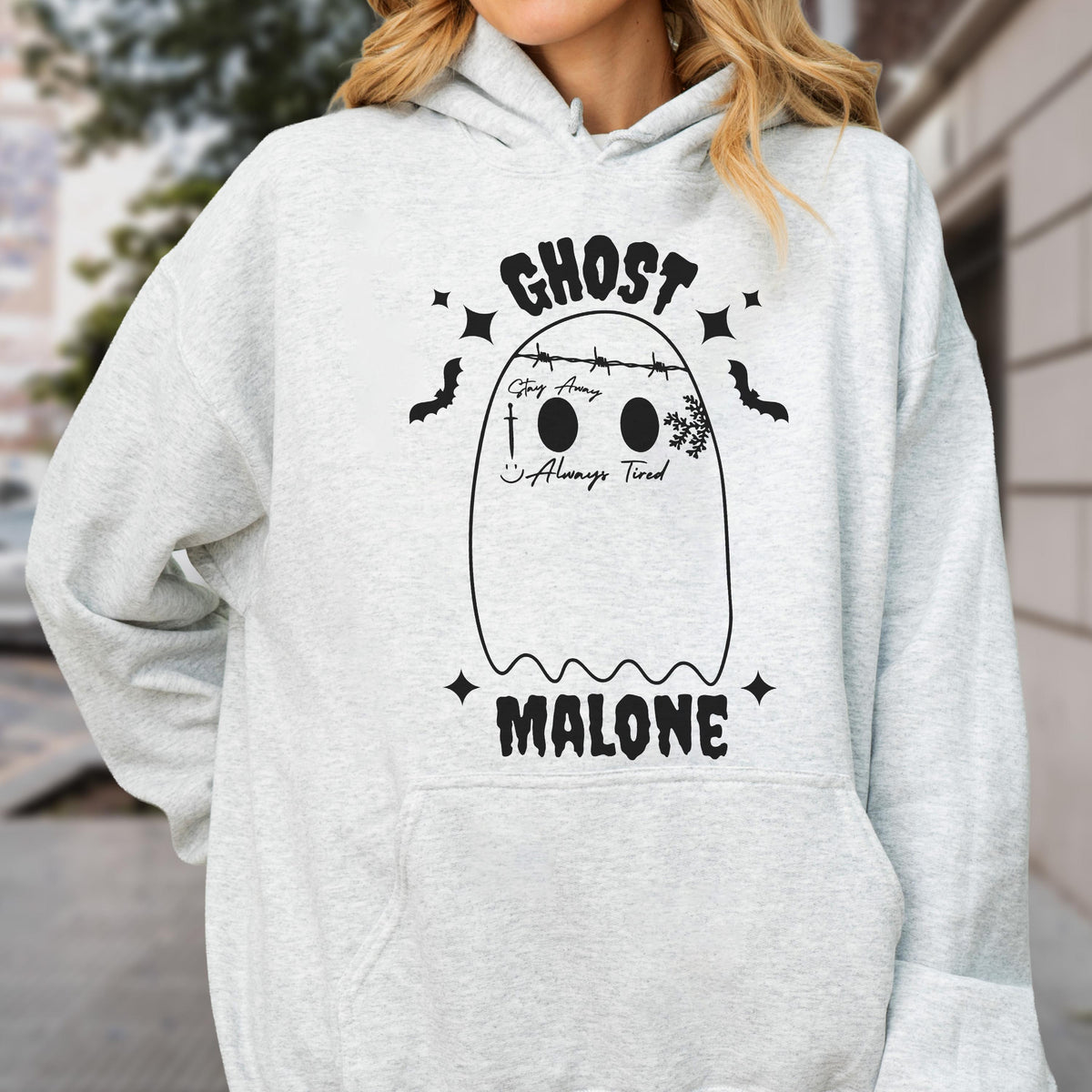 May include: A light gray hoodie featuring a black graphic of a ghost with the text "GHOST MALONE". The ghost design includes the phrases "Stay Away" and "Always Tired". The design is surrounded by stars and bats.