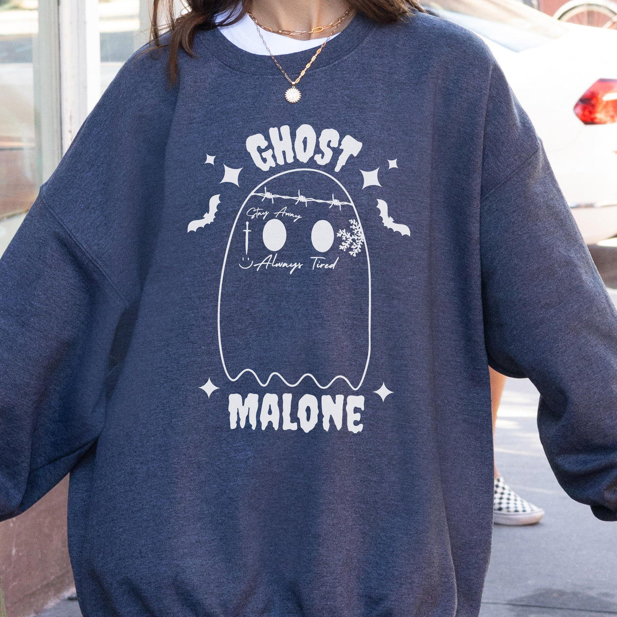 May include: A dark gray sweatshirt with a white graphic of a ghost and the text "GHOST MALONE". The ghost design includes the phrases "Stay Away" and "Always Tired". The sweatshirt has a crew neck and long sleeves.