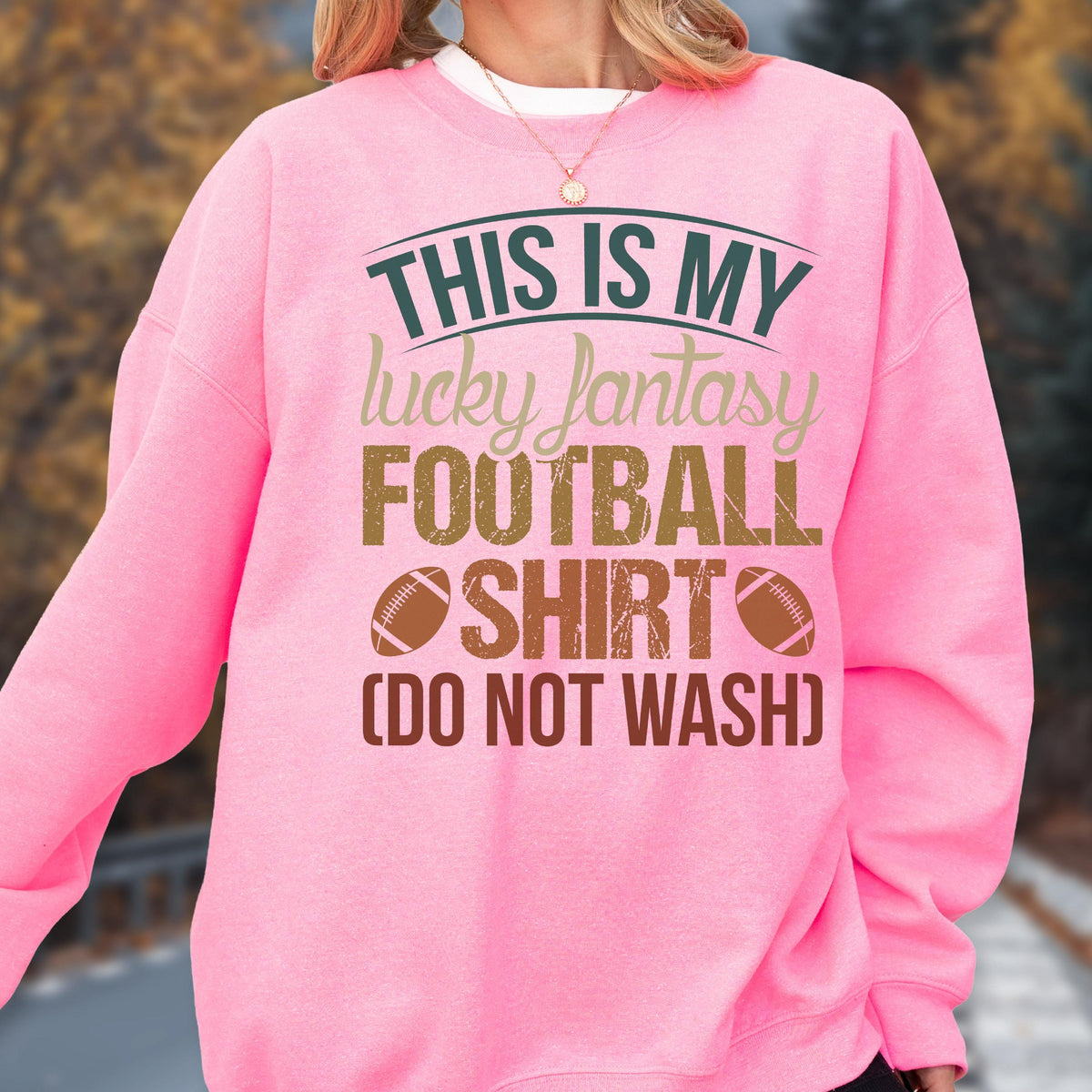 May include: A pink sweatshirt with the text "THIS IS MY lucky fantasy FOOTBALL SHIRT (DO NOT WASH)" in green, tan, and brown. The design includes two football illustrations.