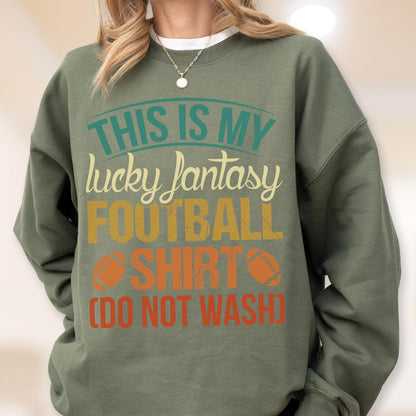 May include: Olive green sweatshirt with the text "THIS IS MY lucky fantasy FOOTBALL SHIRT (DO NOT WASH)". The text is in teal, yellow, orange, and white. Two orange footballs are printed on the shirt.