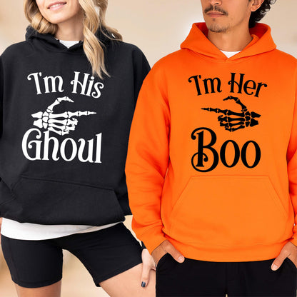 May include: Black and orange Halloween hoodies. The black hoodie says "I'm His Ghoul" with a skeleton hand pointing to the right. The orange hoodie says "I'm Her Boo" with a skeleton hand pointing to the left. Both hoodies have a front pocket.