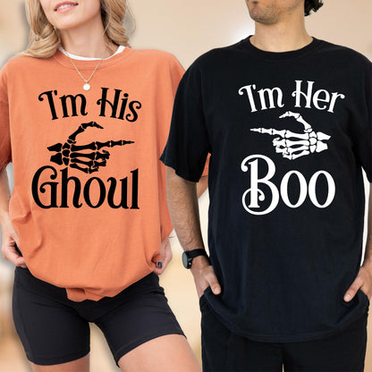 May include: An orange t-shirt with black text reading I'm His GHOUL and a black skeleton hand graphic, alongside a black t-shirt with white text reading I'm Her Boo and a white skeleton hand graphic pointing toward the orange t-shirt.