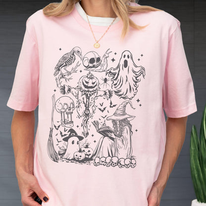 May include: A light pink t-shirt featuring a black and white Halloween-themed graphic. The design includes a crow skeleton, skulls, a ghost, a scarecrow, a witch reading a book, bats, and pumpkins. The shirt has short sleeves and a crew neck.