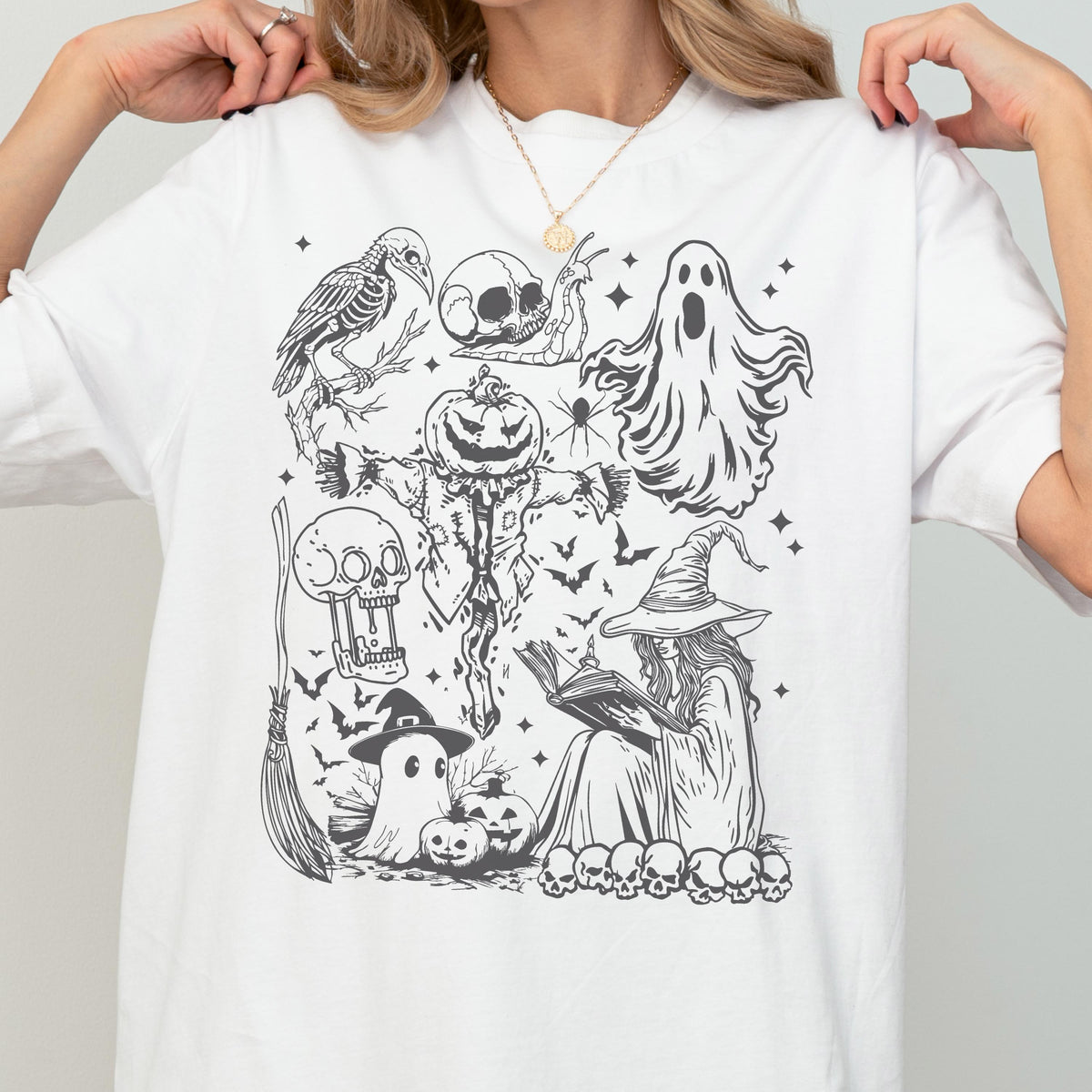 May include: White t-shirt featuring a black and white Halloween-themed graphic. The design includes a skeleton crow, skull, ghost, scarecrow, witch reading a book, bats, and other spooky elements. A fun and festive design for the Halloween season.
