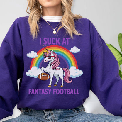 May include: A purple long-sleeve sweatshirt featuring a graphic of a white unicorn with a pink mane, wearing sunglasses and holding a brown football. Behind the unicorn is a colorful rainbow and white clouds. The text reads I SUCK AT FANTASY FOOTBALL.