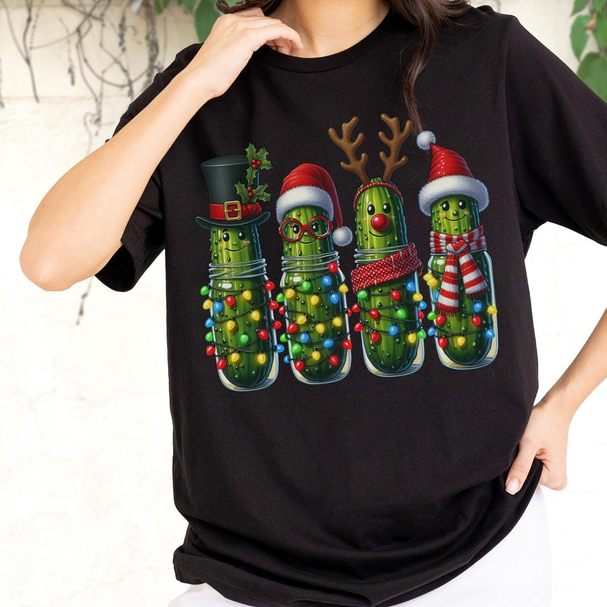 May include: Black t-shirt featuring a festive design of four anthropomorphic pickles in glass jars, each adorned with Christmas accessories like a top hat, Santa hat, reindeer antlers, and a scarf. The pickles are wrapped in colorful Christmas lights.