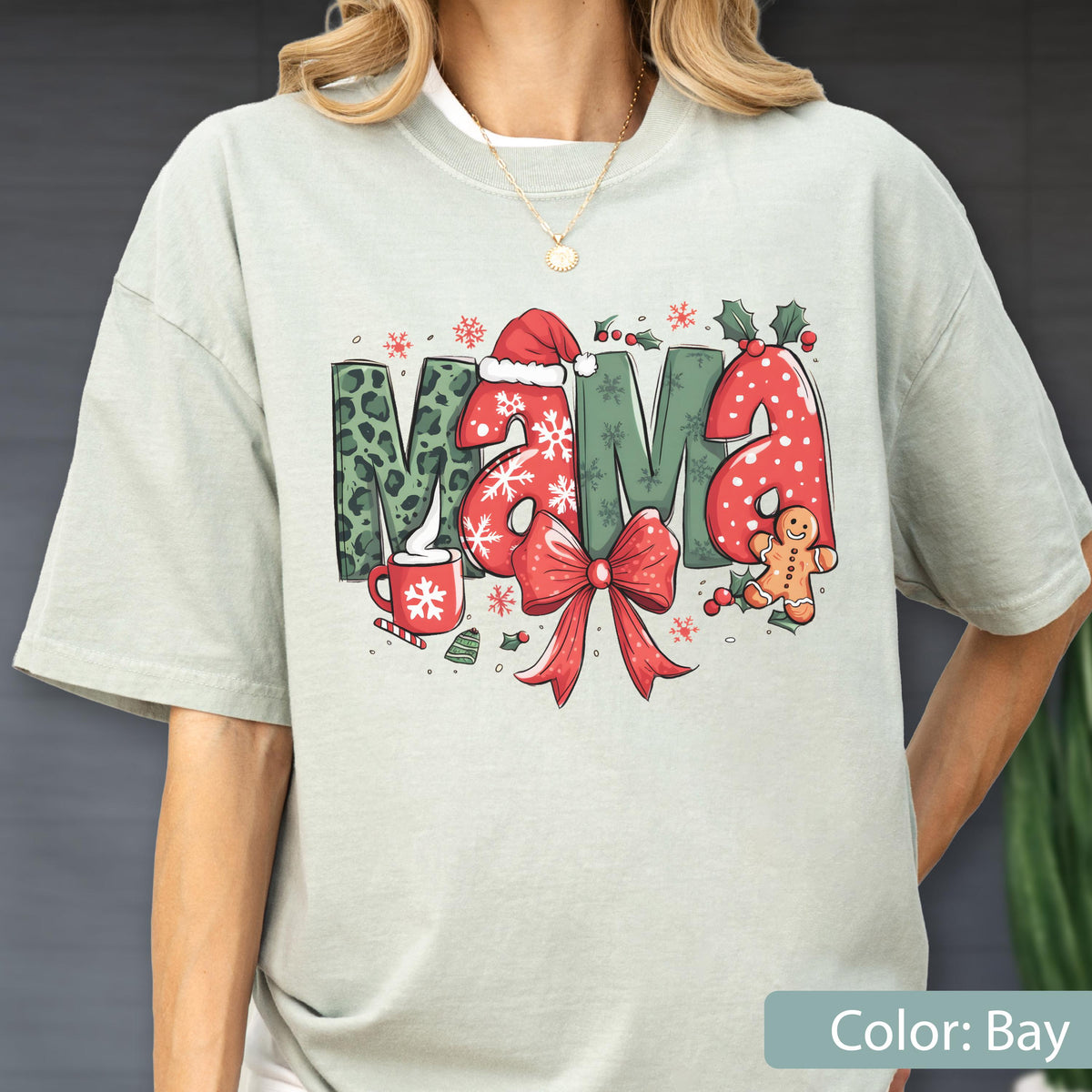 May include: A light green t-shirt with the word "Mama" in a Christmas-themed design. The letters are decorated with leopard print, snowflakes, and a Santa hat. A red bow and gingerbread man are also featured.