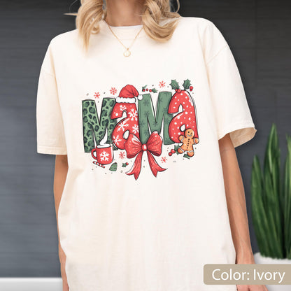 May include: Ivory-colored t-shirt with a festive "MAMA" graphic. The letters feature a mix of patterns, including leopard print and polka dots, with holiday accents like a Santa hat, snowflakes, and a gingerbread man. A red bow and holly complete the design.
