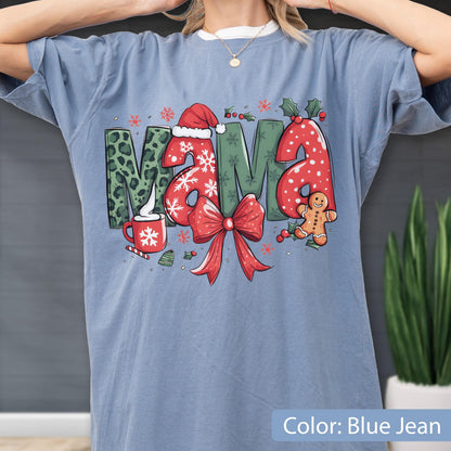 May include: Blue jean colored t-shirt with a Christmas-themed graphic. The word "MAMA" is displayed with festive designs: a Santa hat, snowflakes, a red bow, and a gingerbread man. The shirt also features a cup of hot cocoa.