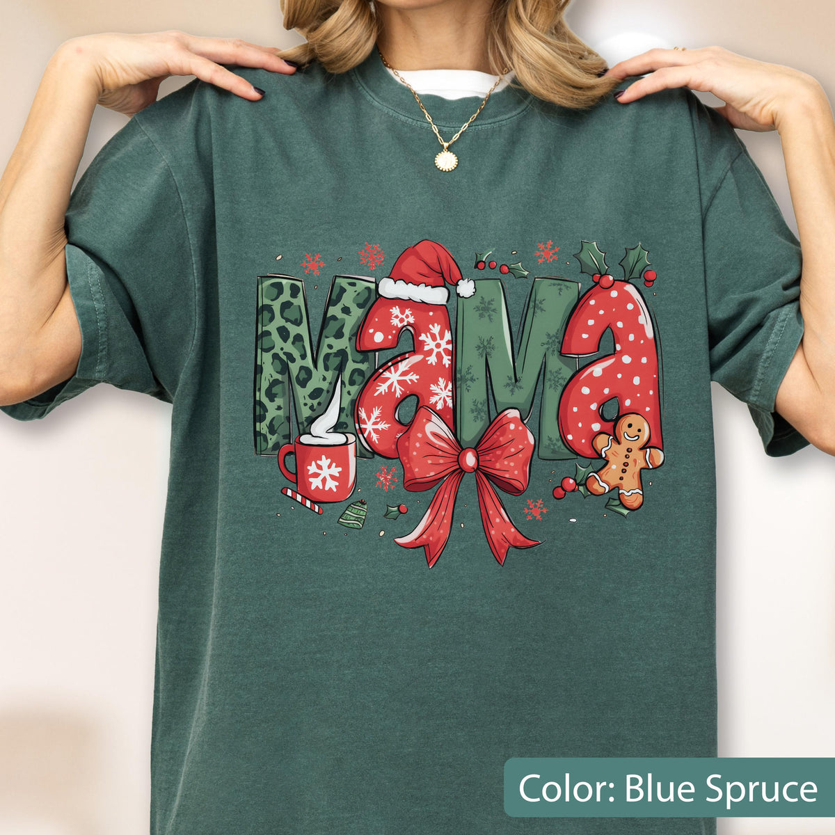 May include: Blue spruce-colored t-shirt with a festive "MAMA" graphic. The letters feature a leopard print, snowflakes, and a Santa hat. A red bow, gingerbread man, and a cup of cocoa complete the holiday design.