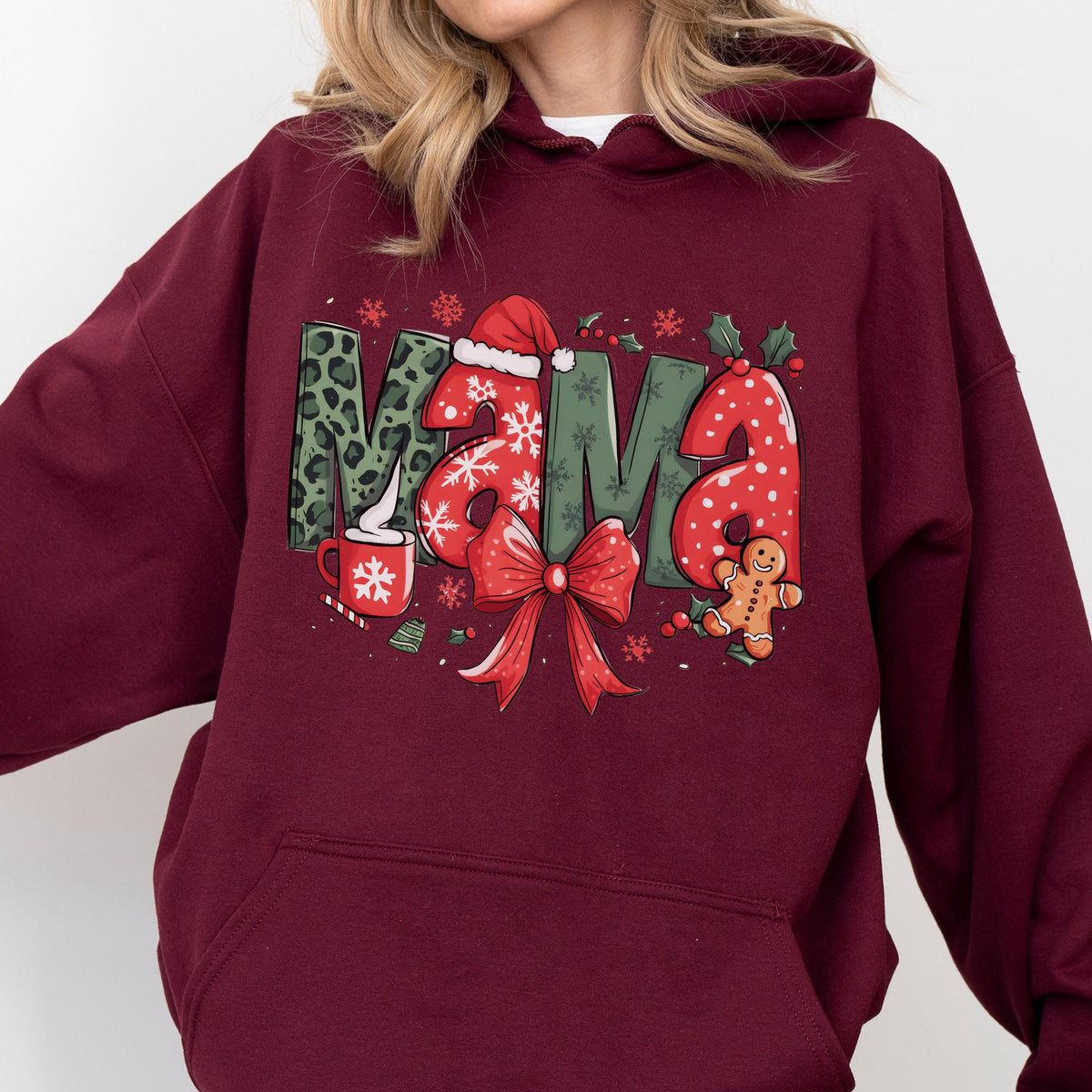May include: Burgundy hoodie with a festive "Mama" graphic. The letters feature leopard print, snowflakes, and polka dots. A Santa hat, bow, gingerbread man, and a cup of cocoa with a snowflake are also included in the design.