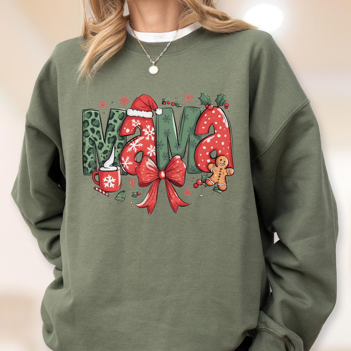 May include: Olive green sweatshirt with the word "Mama" in a festive Christmas design. The letters feature leopard print, snowflakes, and red polka dots. A Santa hat, bow, gingerbread man, and holly complete the holiday theme.