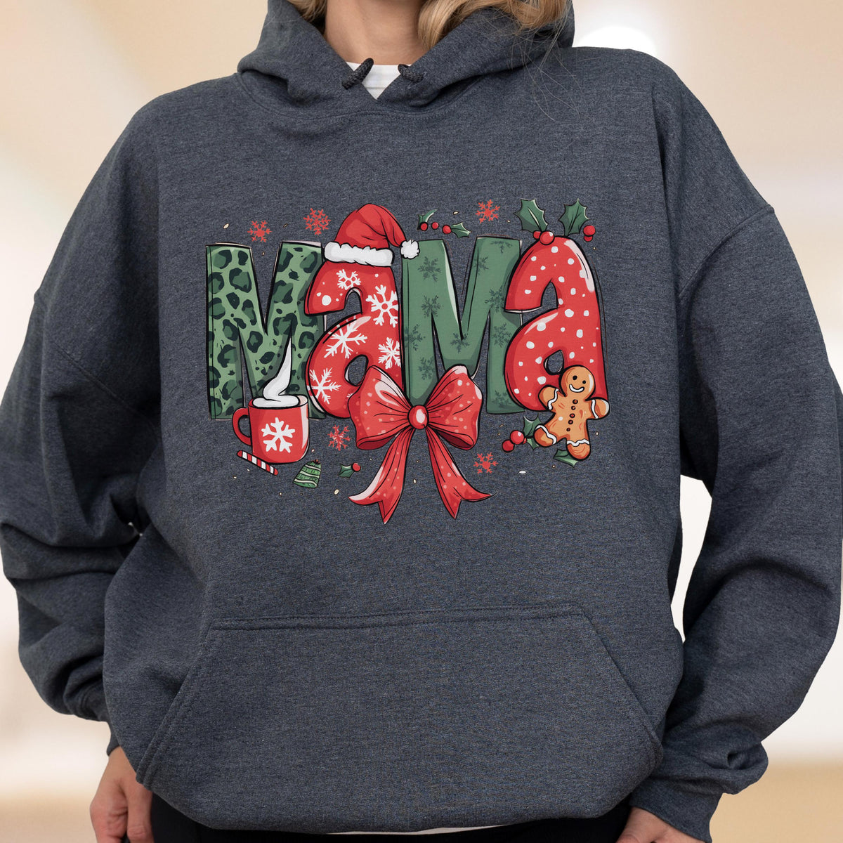 May include: A dark gray hooded sweatshirt featuring the word "MAMA" in a festive Christmas design. The letters are decorated with leopard print, snowflakes, and a red bow. A gingerbread man and a mug of hot cocoa complete the holiday theme.