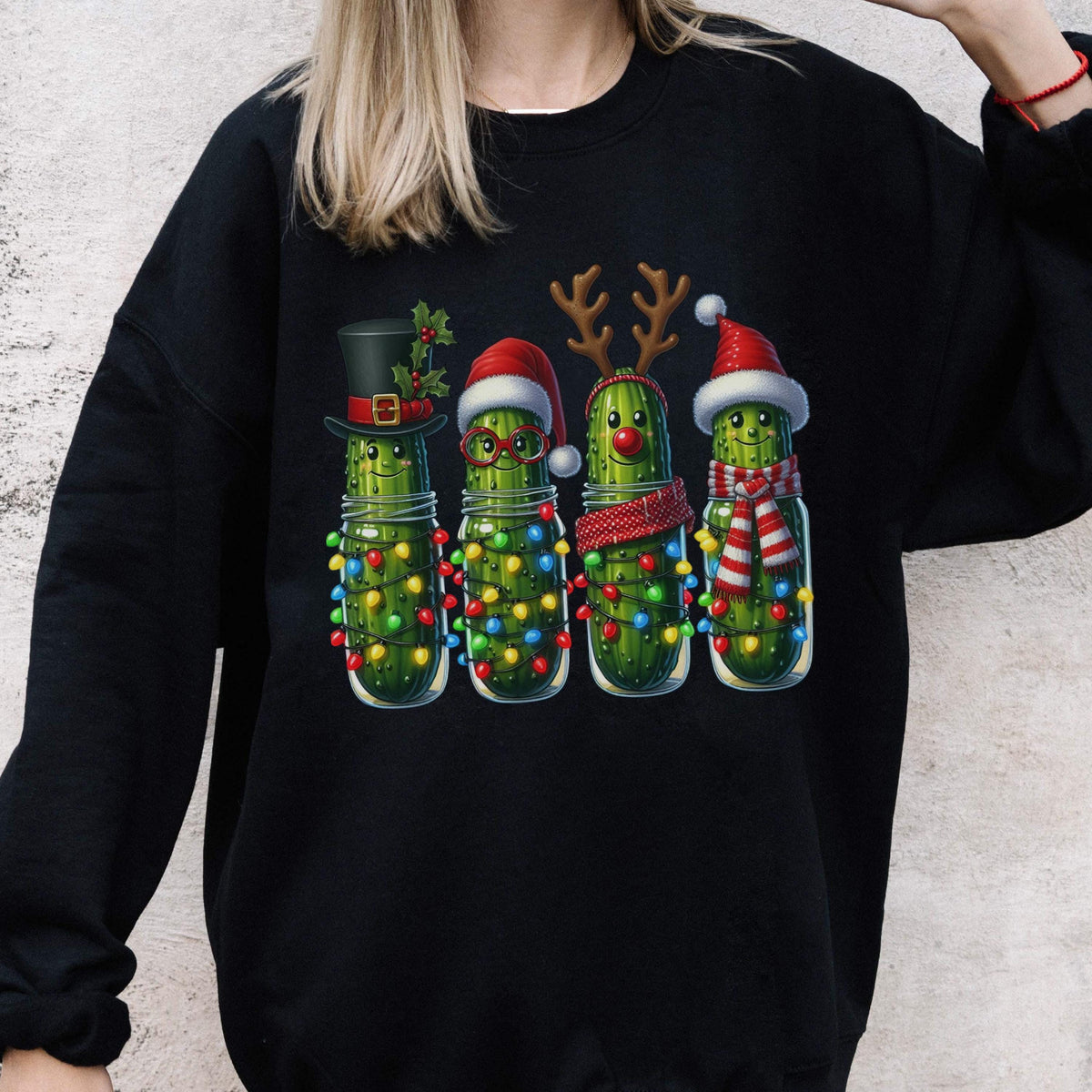 May include: A black long-sleeve sweatshirt featuring a graphic print of four green pickles in glass jars. Each pickle is decorated for the holidays with items like a top hat, Santa hat, reindeer antlers, a red scarf, and colorful string lights.