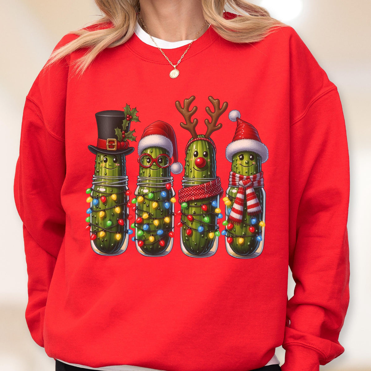 May include: A bright red crewneck sweatshirt featuring a graphic print of four green pickles in glass jars. Each pickle is decorated for the holidays with items including a top hat, Santa hat, reindeer antlers, a red nose, and colorful string lights.