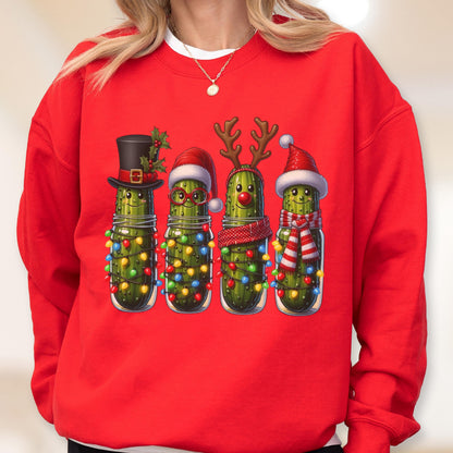 May include: A bright red crewneck sweatshirt featuring a graphic print of four green pickles in glass jars. Each pickle is decorated for the holidays with items including a top hat, Santa hat, reindeer antlers, a red nose, and colorful string lights.