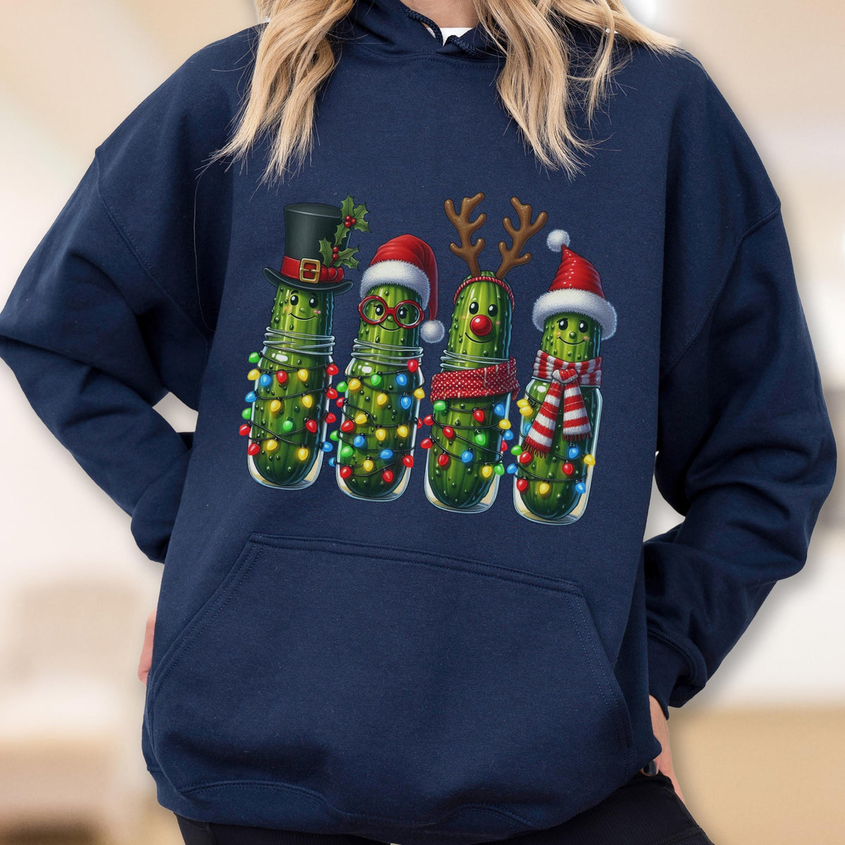 May include: A navy blue hooded sweatshirt featuring a graphic print of four green pickles decorated for the holidays. The pickles wear festive accessories including a top hat, Santa hats, reindeer antlers, and scarves, all wrapped in colorful string lights.