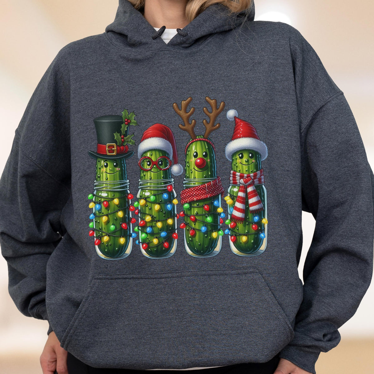 May include: A dark heather gray hooded sweatshirt featuring a graphic of four green pickles in glass jars. Each pickle is decorated for the holidays with items including a top hat, Santa hat, reindeer antlers, red nose, glasses, and colorful string lights.