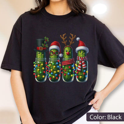 May include: A black t-shirt featuring a graphic of four green pickles in glass jars. Each pickle is decorated for the holidays with items including a top hat, a Santa hat, reindeer antlers, a red nose, and colorful Christmas string lights.