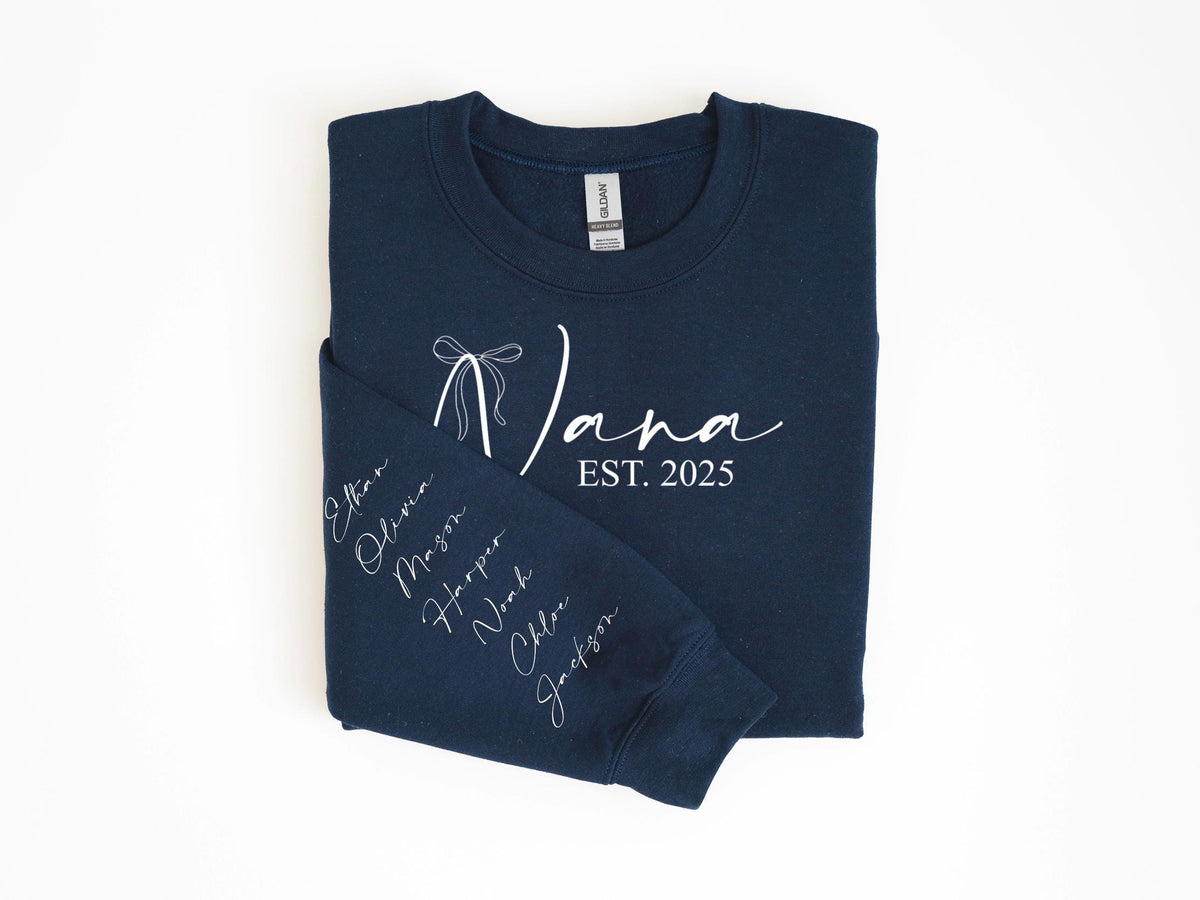 May include: Navy blue sweatshirt with the word "Nana" in white script, a bow graphic, and "EST. 2025". The left sleeve displays names in white script. A cozy, personalized gift.