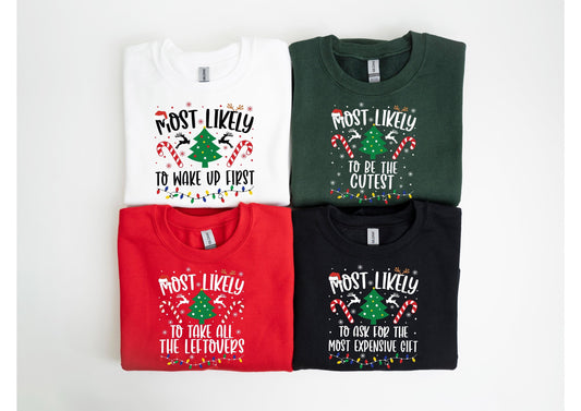 May include: Four Christmas-themed sweatshirts in white, green, red, and black. Each shirt has a festive design with the words "MOST LIKELY" above a Christmas tree and candy canes, with different phrases below, such as "TO WAKE UP FIRST."