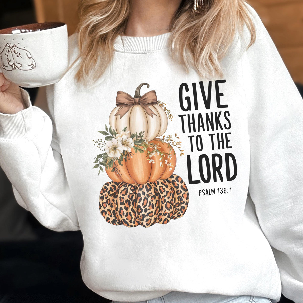 May include: White sweatshirt featuring a stacked pumpkin design with a leopard print base, orange and white pumpkins, and floral accents. The text "GIVE THANKS TO THE LORD" is printed on the right side.